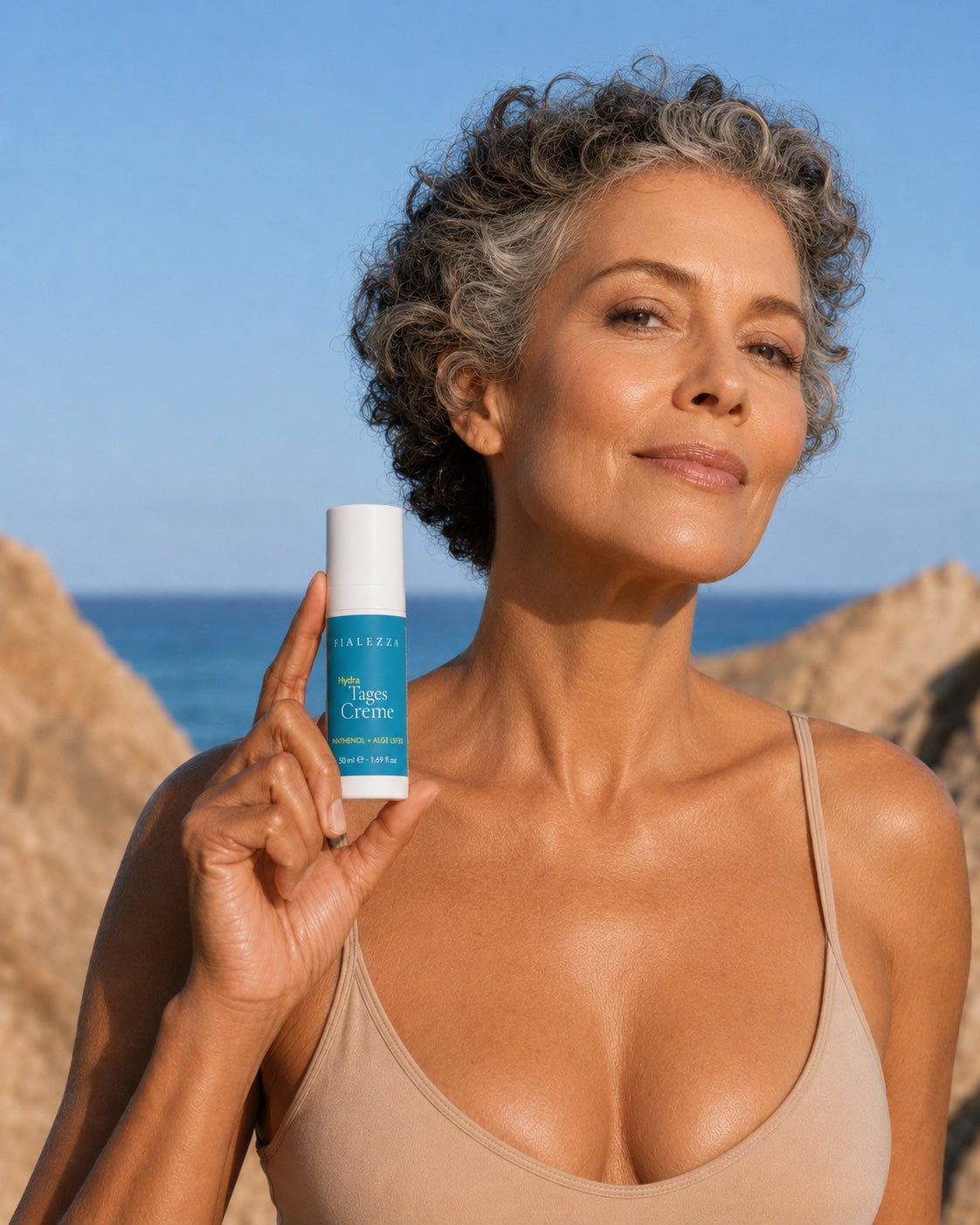Frau mit grauem Lockenhaar hält die Fialezza Hydra Tages Creme vor Felsen und Meer