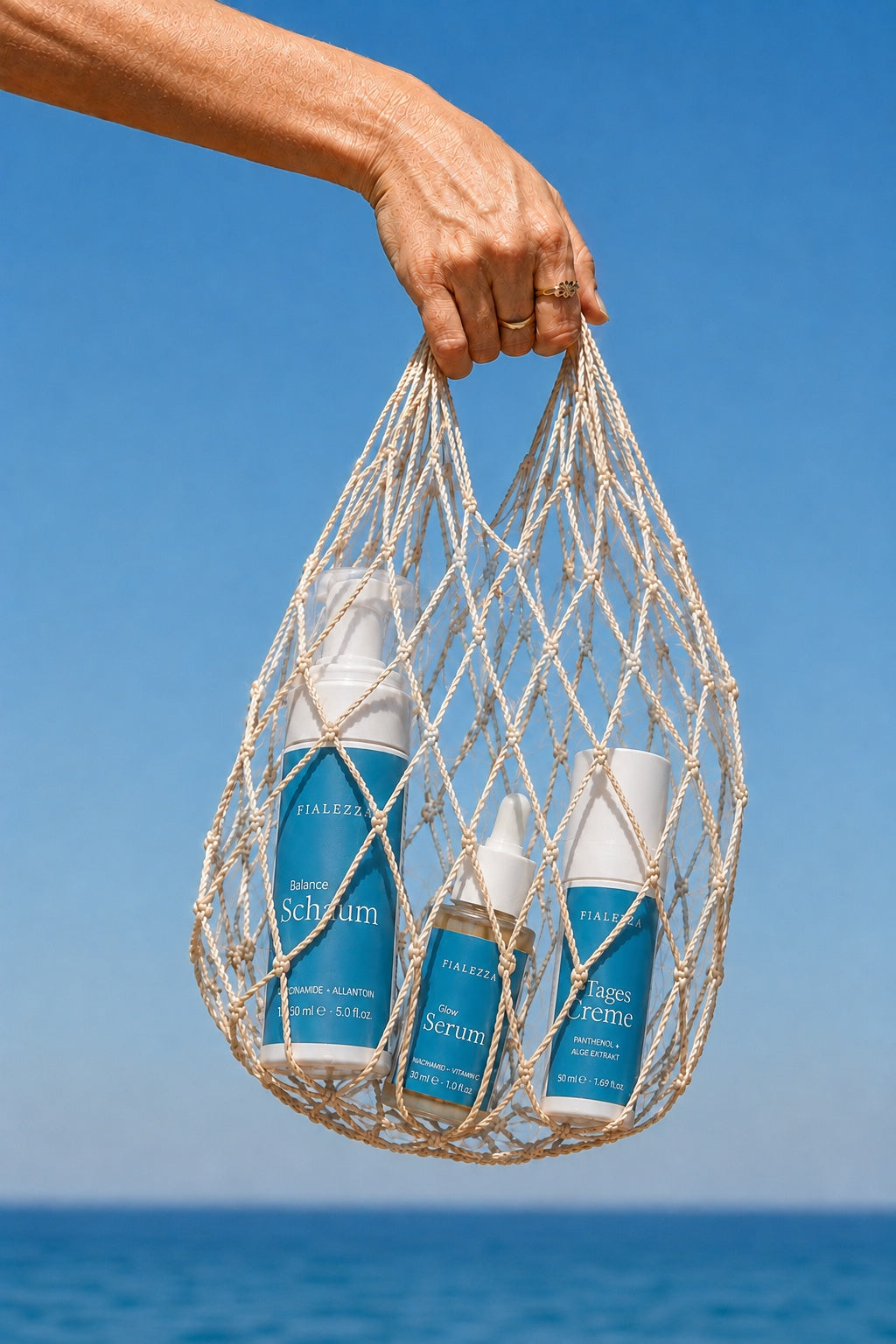 Eine Hand hält die drei Fialezza Produkte in einem Netzbeutel vor blauem Himmel und Mittelmeer