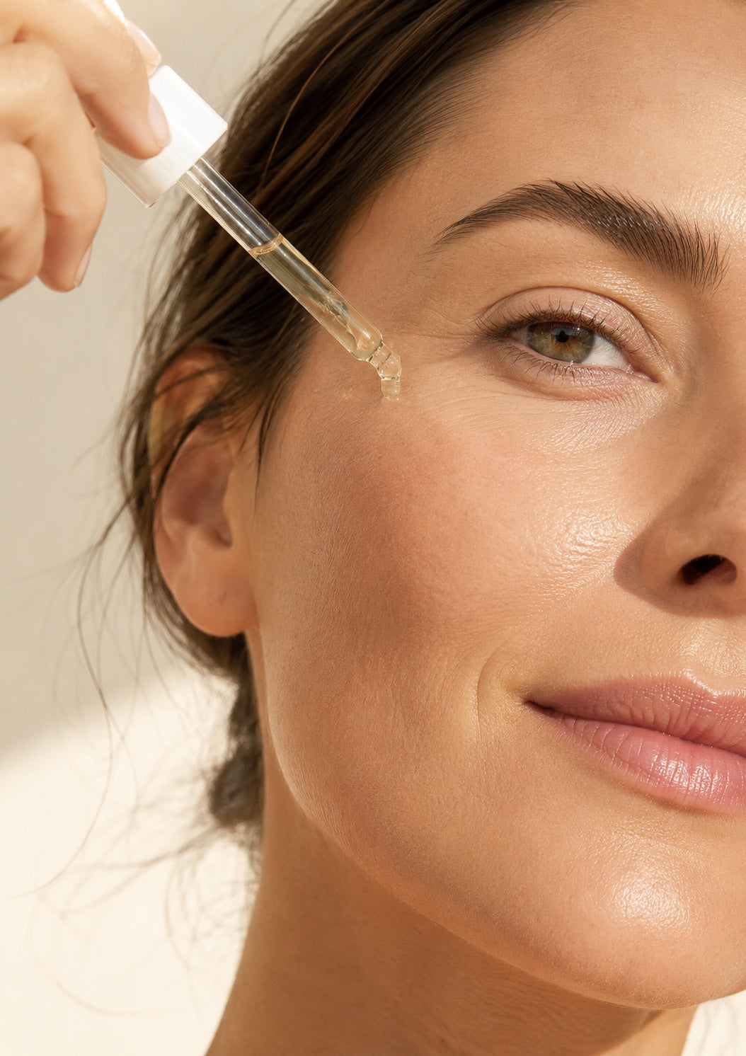 Pipette mit einem Tropfen Fialezza Glow Serum an der Wange einer Frau